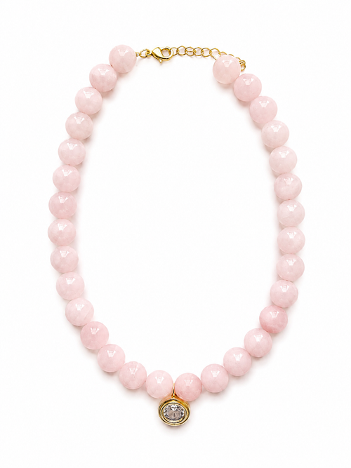 A pink faceted bead necklace with a gold-tone clasp and a small round gold pendant featuring a clear stone, displayed on a clean white background.