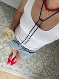 Person wearing a white tank top with a unique back design, holding a glass, and standing on a patterned rug. – view 2