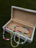 Open jewelry box with colorful beaded necklaces on a green grass background – view 2